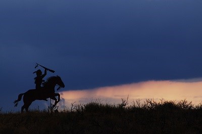 A metal silhouette of a Nez Perce warrior on horseback with the sunset behind.