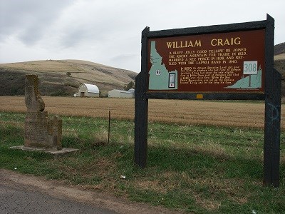 A dark brown sign with 'William Craig' next to a monument shaped like Idaho.